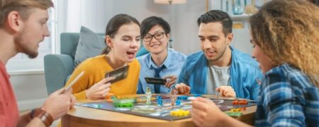 Fem vänner spelar ett brädspel tillsammans runt ett bord