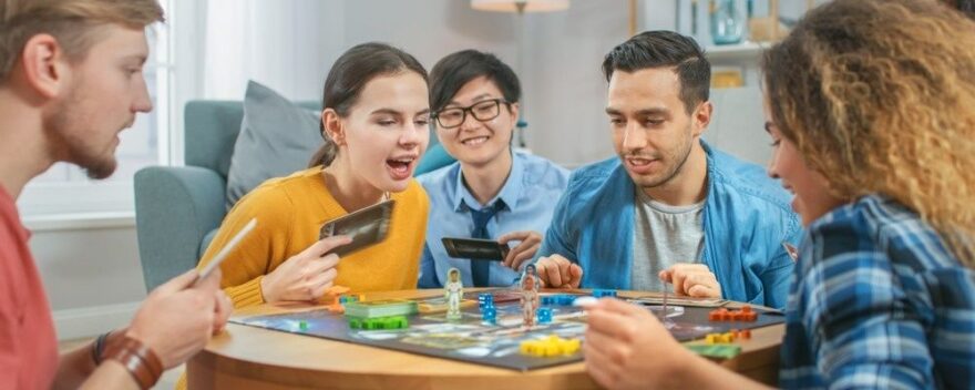Fem vänner spelar ett brädspel tillsammans runt ett bord